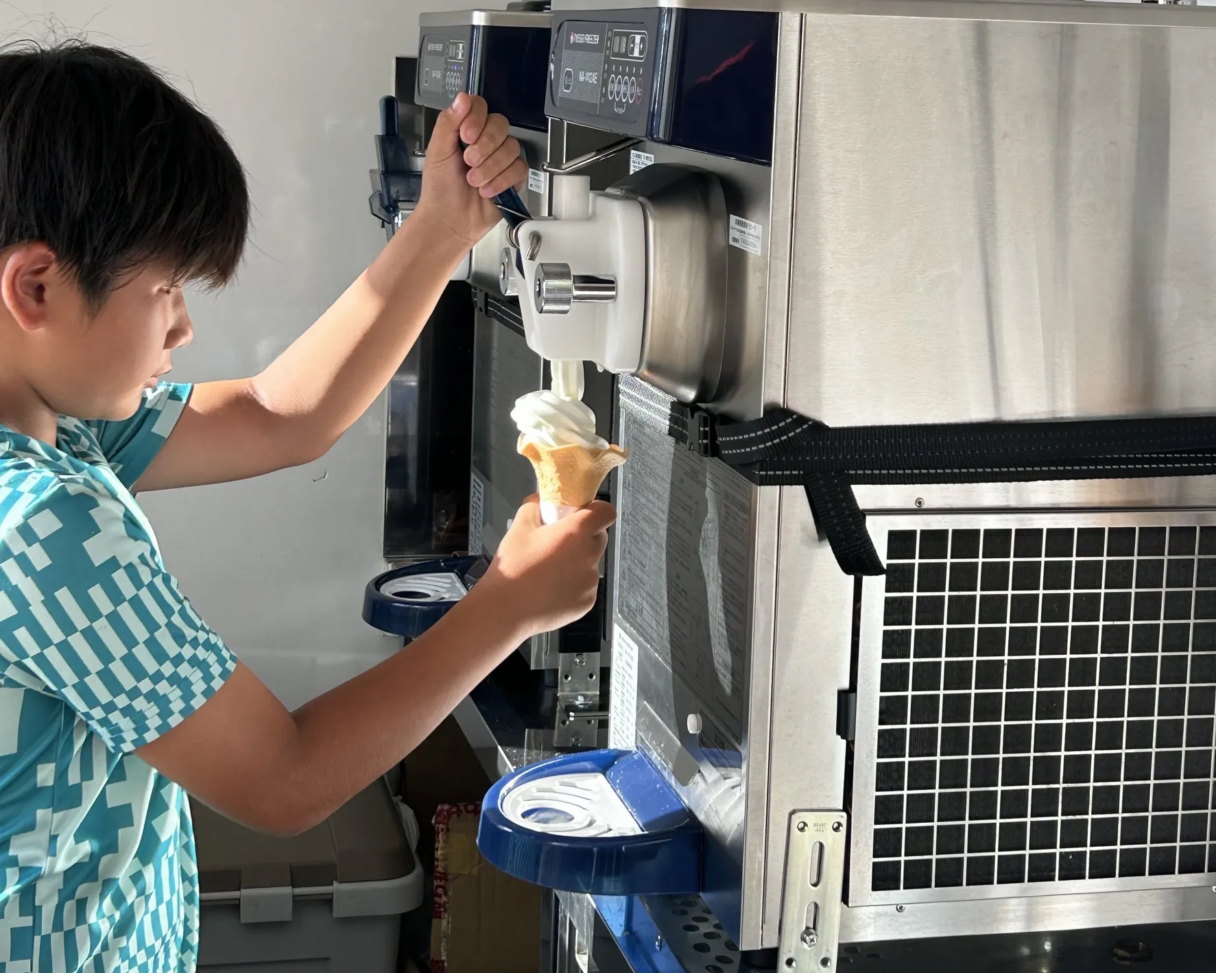 キッチンカーの機械でソフトクリーム作りを体験する少年